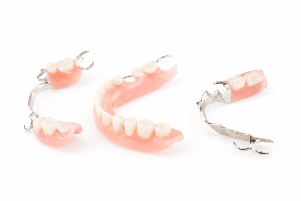 an image of threw partial dentures on a white background for dentures vs. implants blog