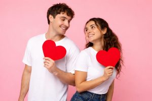 Couple holding red hearts, smiling on valentine's day date night, sharing tips to prevent bad breath